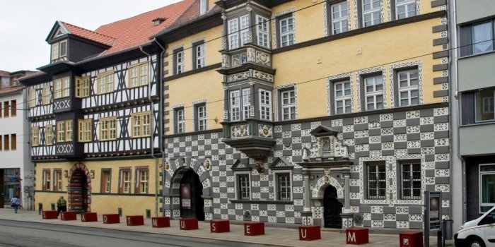 Sicht auf die reich verzierte Fassade eines Hauses und davorstehende rote Würfel, die das Wort Stadtmuseum ergeben