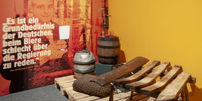 Bierfässer aus Holz und Aluminium, Holzbretter (Dauben) und Zitat auf Wand