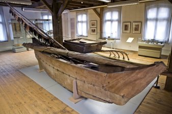 Ein Boot aus Holz, im Hintergrund hohe und flache Vitrinen. Alles auf einem Holzfußboden.