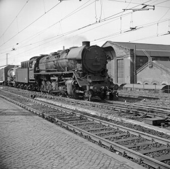 Schwarz-Weiß Motiv mit einer Lokomotive auf den Gleisen im Bahnhof stehend mit Gebäuden im Hintergrund