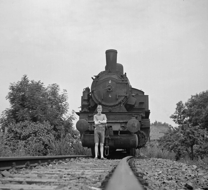 Schwarz-Weiß Motiv mit einem jungen Mann vor einer Lokomotive auf den Gleisen stehend
