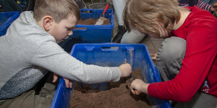 zwei Kinder buddeln in einer Kiste mit Sand