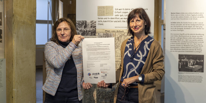 zwei Frauen halten ein bedrucktes Blatt Papier in die Höhe