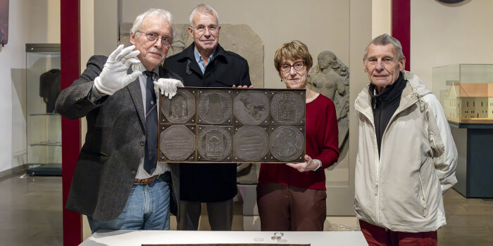 vier Personen, zwei davon halten eine Platte mit vier Medaillenmotiven in der Hand