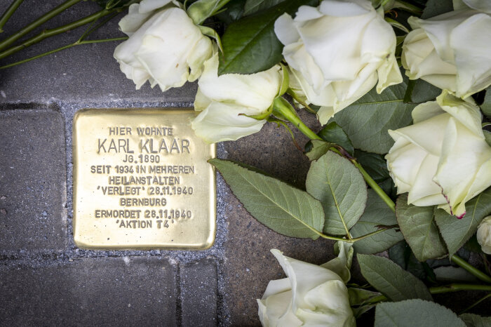Verlegung des ersten Stolpersteins ein Messing-Gedenkstein mit Inschrift und niedergelegten weißen Rosen