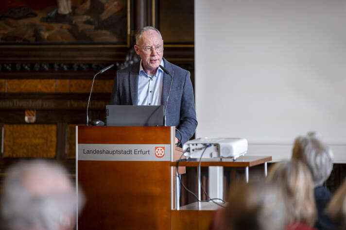 an einem Rednerpult steht an Mann mit Brille und spricht ins Mikrofon