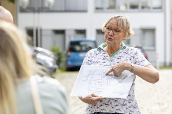 eine Frau mit Brille und kurzen blonden Haaren hält einen Lageplan in der Hand