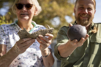 zwei Personen halten archäologische Funde in der Hand: einen Teil eines tierischen Kiefers und ein rundes Gefäß