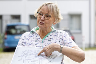 eine Frau mit Brille und kurzen blonden Haaren hält einen Lageplan in der Hand