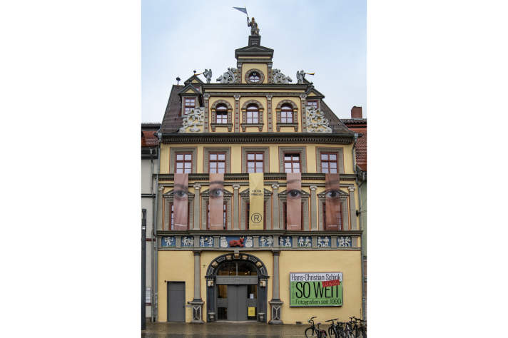 Banner mit Augen und Gesichtern an Fassade eines gelben verzierten Gebäudes
