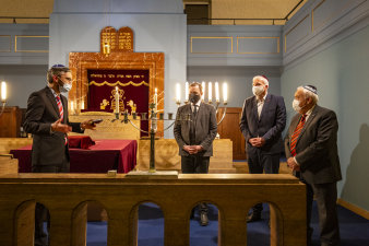 vier Männer, die die jüdische Kopfbedeckung Kippa tragen, entzünden den Chanukka-Leuchter in einer Synagoge