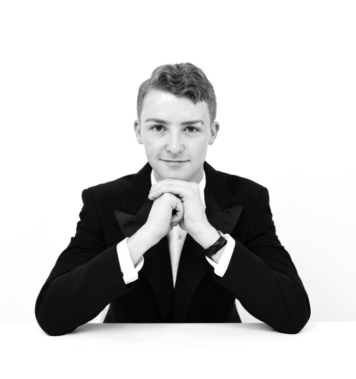 Schwarz Weiß Porträt von einem jungen Mann im Anzug der mit den Händen sein Kinn stützt 