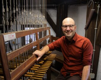 Mann mitteleren Alters in einem roten Hemd, mit Brille und wenig Haaren an einem Carillon-Spieltisch sitzend