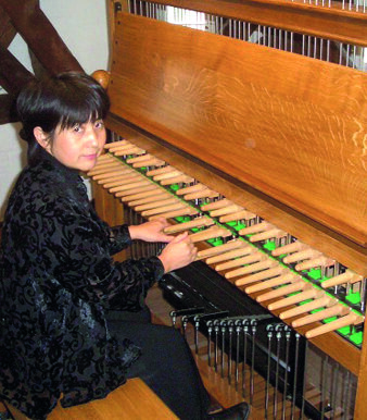 Eine japanische Glockenspielerin mittleren Altes sitzt am Stockenklavier eines Carillon-Spieltisches