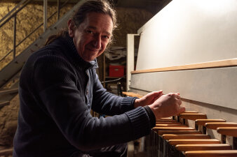 Fröhlich gestimmter Mann mittleren Alters im dicken Pullover an den Tasten eines Stockenklaviers