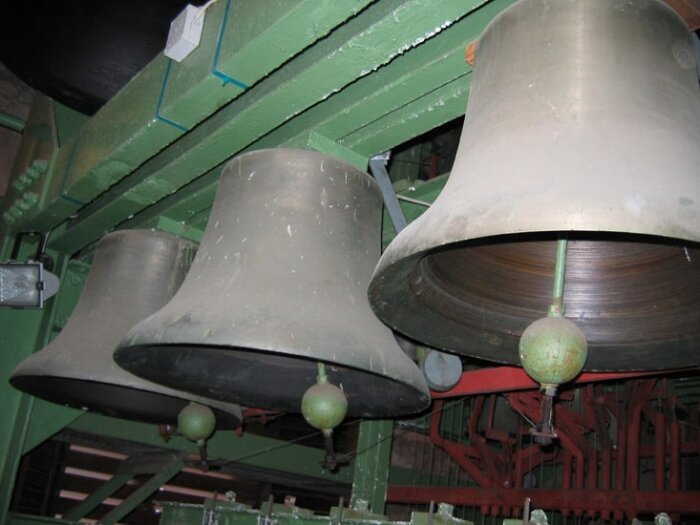 Drei große Glocken in einer grünen Metallvorrichtung hängend