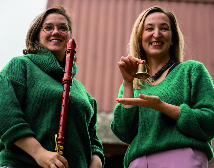 Das polnische Duo „Wood & Bronze“ Zwei Frauen mittleren Alters in grünen Pullovern halten eine Blockflöte und eine Glocke im Miniformat