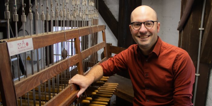 Foto: Carillonneur Tijl Stynen am Spieltisch © Privataufnahme Mann mitteleren Alters in einem roten Hemd, mit Brille und wenig Haaren an einem Carillon-Spieltisch sitzend