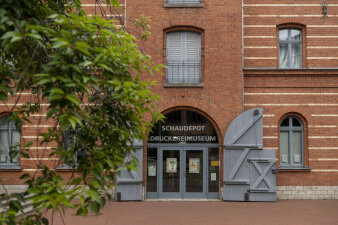 Rotes Backsteingebäude mit großen, grauen Flügeltoren als Eingang