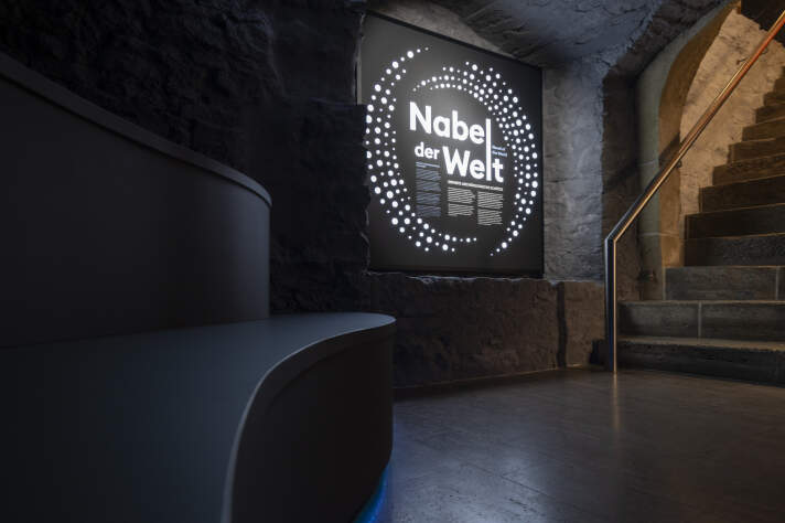 Grafik mit Leuchtschrift an einer Wand, Schriftzug "Nabel der Welt"
