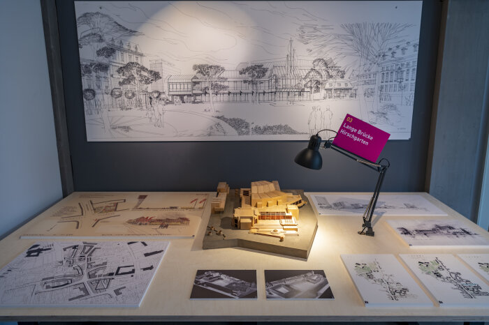 Blick in einer Ausstellung, auf dem Tisch und an der Wand befinden sich Pläne, in der Mitte ein Stadtmodell