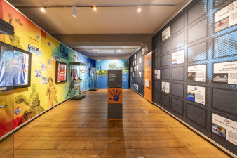 Ausstellungsraum mit Bunden Wänden und einer grau-orangefarbenen Stele in der Mitte