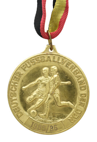 Goldmedaille mit Prägung zweier Fussballspieler, die um einen Ball kämpfen und Inschrift „Deutscher Fußballverband der DDR 1985/1986“