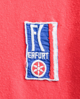 Ein gestickter „FC Rot-Weiß Erfurt“-Aufnäher mit weißen Buchstaben auf blauem Grund, rot-weißen Streifen.
