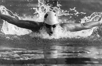 Eine Leistungsschwimmerin mit Badekappe und Schwimmbrille beim Schmetterlingsschwimmen im Schwimmbecken.