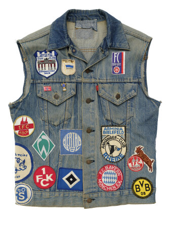 Eine Jeansweste mit vielen verschiedenen Fußball-Stick-Aufnähern und Vereins-Pins.