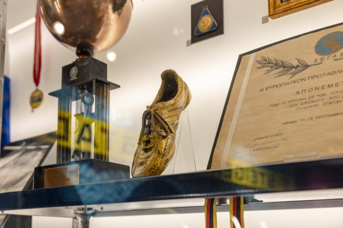 in einer Vitrine befinden sich mehrere Exponate, mittig ein goldfarbener Sportschuh mit Signatur