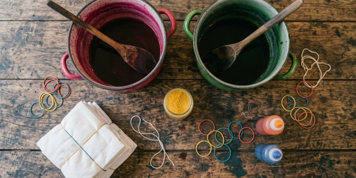 Zwei Töpfe mit Holzlöffel, Stoffballen, Farben und Gummis zum Stoffe färben