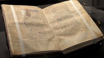 Seiten einer alten Pergamenthandschrift mit farbigen Verzierungen und Abbildung eines Mannes mit Buch in einem U