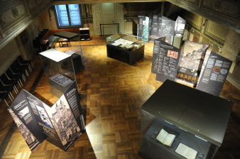 Blick in einen Saal mit Holzboden. Im Raum stehen Ausstellungstafeln und Vitrinen mit alten Büchern und Dokumenten
