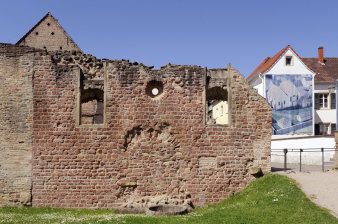 Eine Backsteinmauer mit einer zugemauerten Tür, darüber zwei Rundbogenfenster mit einem runden Fenster dazwischen. 
