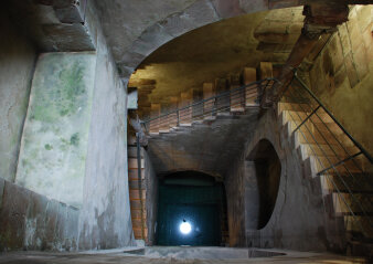Ein dunkler Raum mit einer abfallenden Treppe und einem Lichtpunkt in der Tiefe