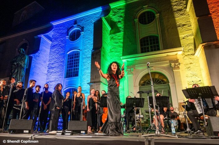 Caravan Orchestra and Choir Ein Ensemble jüdischer Musiker:innen bei einem Auftritt vor einem bunt beleuchteten Gebäude