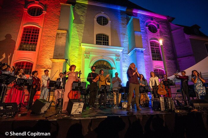 YAM Ensemble Ein Ensemble jüdischer Musiker:innen mit Instrumenten bei einem Auftritt vor einem bunt beleuchteten Gebäude