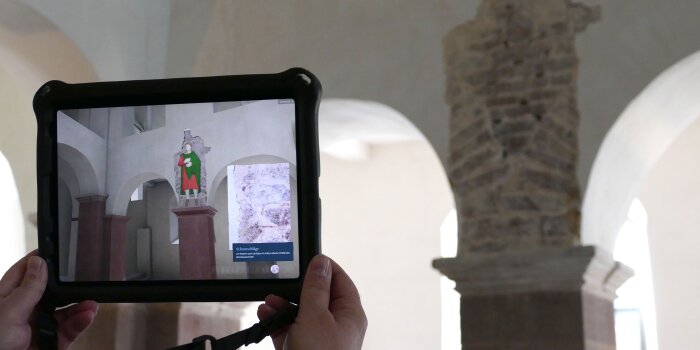 Raum in einer Abteikirche mit einem Tablet mit Augmented Reality-Darstellung der Stuckfiguren