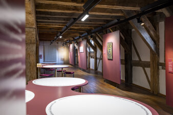 Blick in einen Ausstellungsraum mit Stellwänden und abgerundeten Tischen
