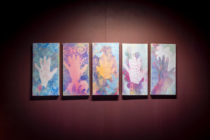 Fünft Bilder mit bunten Händen an einer rotbraunen Wand