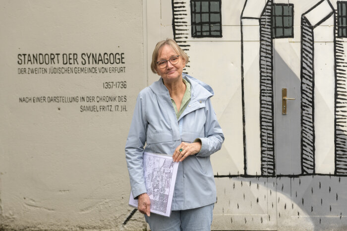 Frau mit Brille und Jacke hält einen Stadtplan vor einer bemalten Mauer