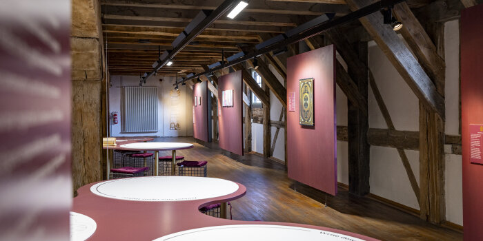 Blick in einen Ausstellungsraum mit Stellwänden und abgerundeten Tischen