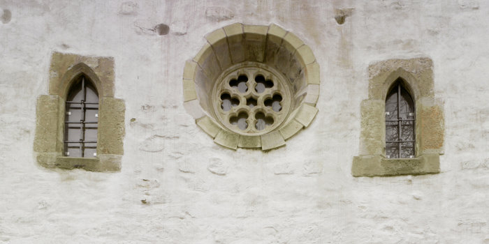 Fassadenausschnitt. Ein großes, rundes Rosettenfenster wird von zwei kleineren Lanzettfenstern flankiert