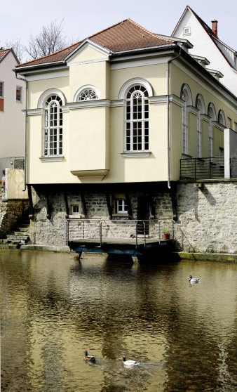 Fassade der Kleinen Synagoge zum Fluß hin. Klassizistisches gelbes Gebäude mit großen, schmalen Fenster mit Rundbogen.