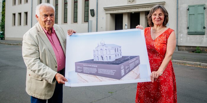ein Mann und eine Frau halten einen Plan, auf dem ein Denkmal eines Gebäudes abgebildet ist