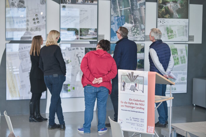 Besucher/-innen in der Ausstellung „Ein Gedenkort für die Opfer des NSU am Thüringer Landtag“ Fünf Personen, die sich die Ausstellung, ein Gedenkort anschauen
