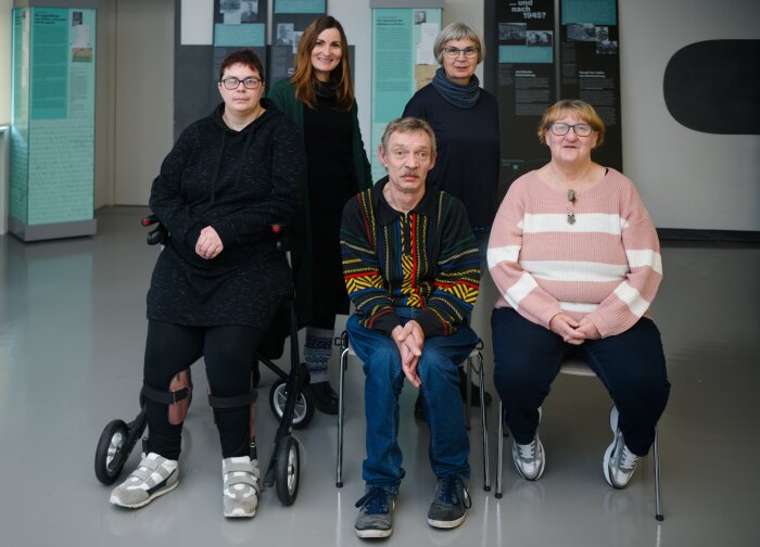 Fünf Personen sitzend und stehend in Ausstellung blicken in die Kamera