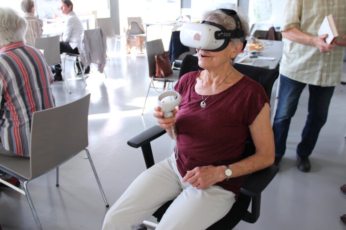 Ältere Frau sitzt auf einem Stuhl mit VR-Brille