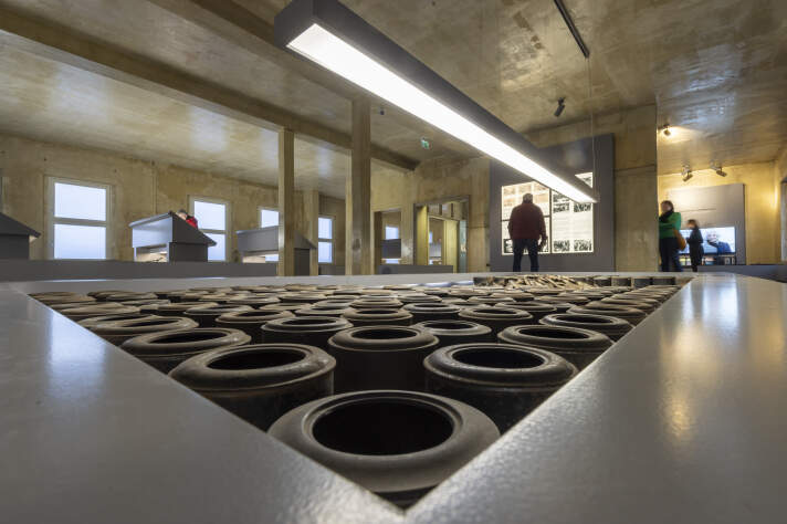 Ausstellungsraum mit industriellem Ambiente und verschiedenen Schaukästen, Installationen und Besuchern